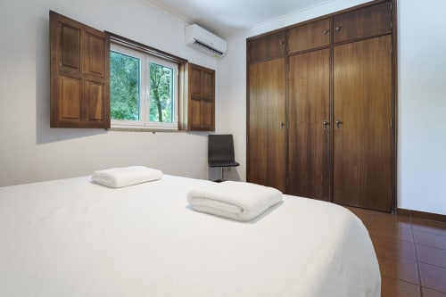 Quarto da casa rural Quinta de Carvalhal em Guimarães com roupa de cama branca, guarda-roupa em madeira e janela com vista para o jardim