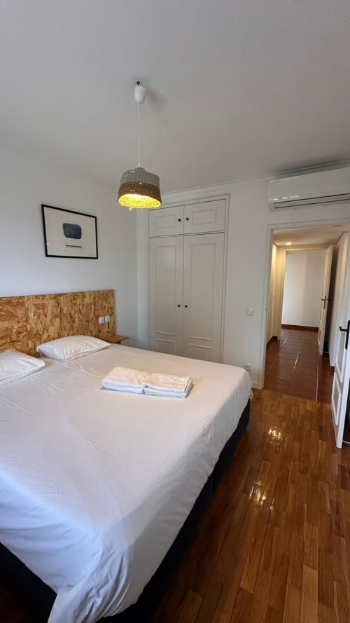 Quarto luminoso na quinta de Carvalhal em Guimarães com roupa de cama branca, cabeceira em cortiça, luminária pendente e madeira