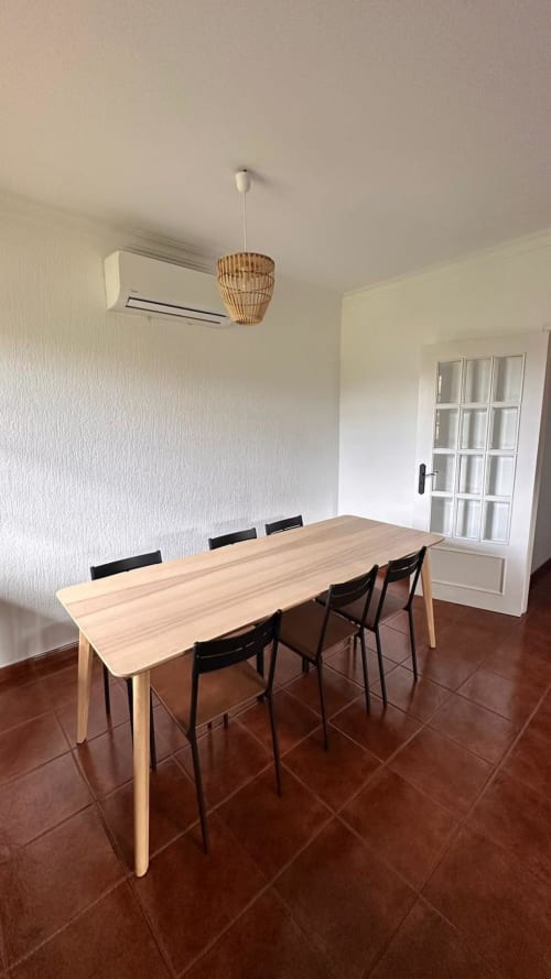 Sala de jantar moderna da Quinta de Carvalhal em Guimarães com mesa de madeira, cadeiras pretas, luminária suspensa tecida e ar condicionado