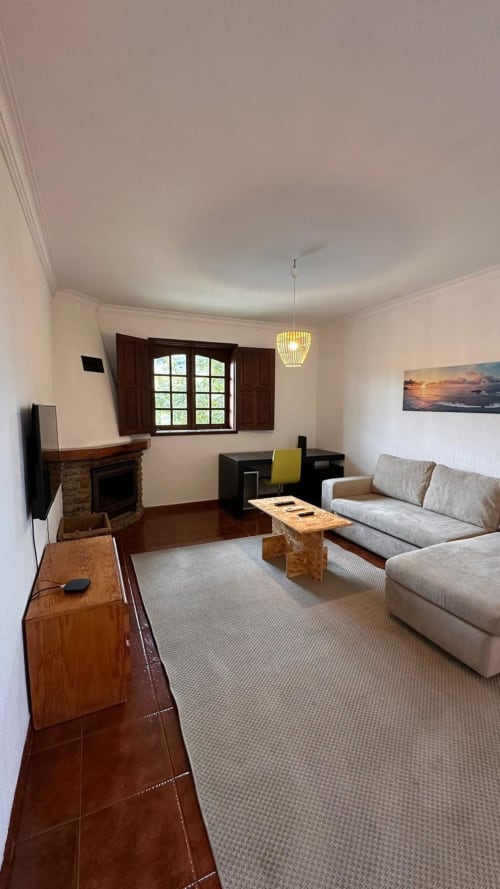 Sala espaçosa da quinta de Carvalhal em Guimarães com sofá bege, lareira e janelas com vista para o jardim