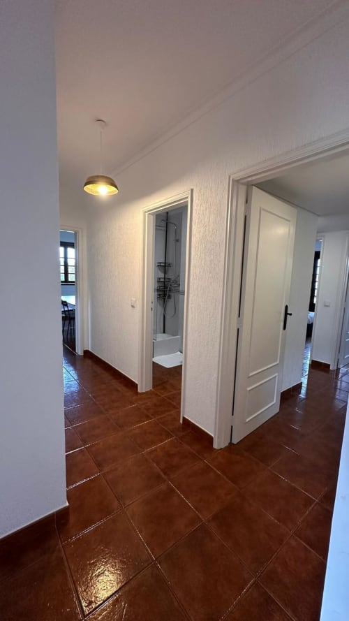 Corredor moderno da casa de campo Quinta de Carvalhal com piso de azulejos marrom, portas brancas e iluminação pendente levando ao chuveiro