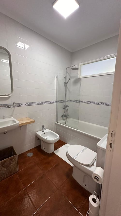 Banheiro moderno da Quinta de Carvalhal com azulejos brancos, chuveiro de vidro, sanitário, bidê e piso em madeira em Guimarães