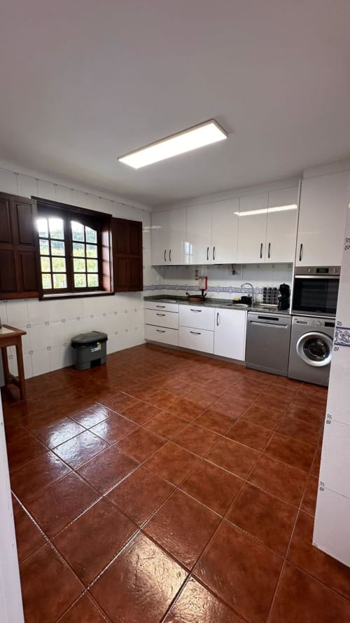 Cozinha moderna na Quinta de Carvalhal em Guimarães com armários brancos, eletrodomésticos em aço inoxidável e tons de terracota