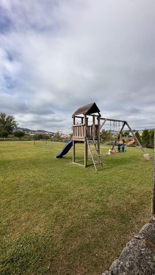 Parque infantil de madeira com escorregador e baloiços no jardim relvado da Quinta de Carvalhal em Guimarães, Portugal