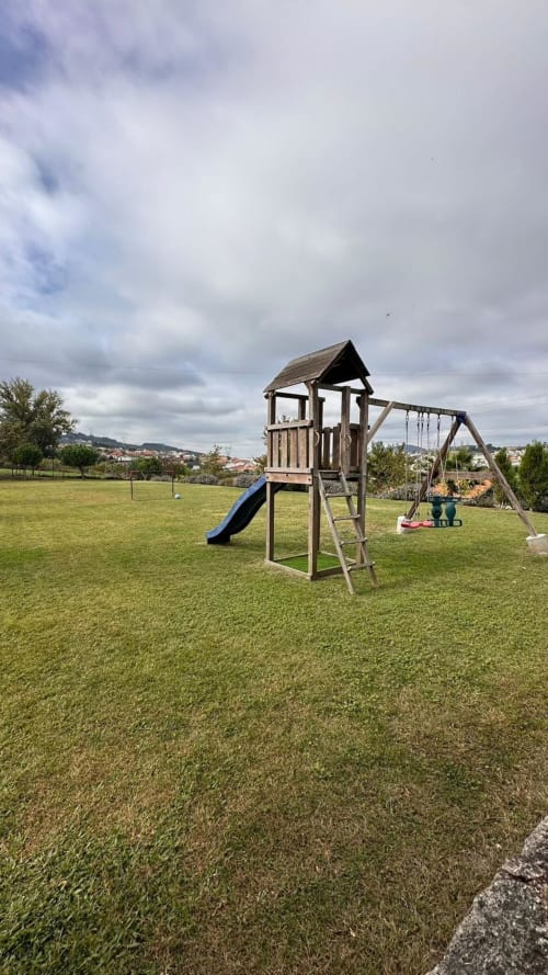 Equipamento de playground em madeira com escorregador e balanços no gramado da Quinta de Carvalhal em Guimarães