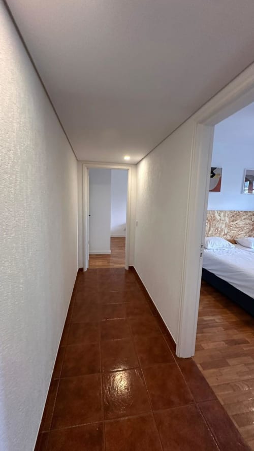 Corredor moderno da Quinta de Carvalhal em Guimarães com piso em azulejo escuro e paredes brancas levando ao quarto