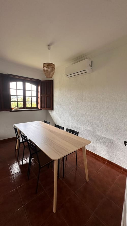 Sala de refeições da Casa de Hóspedes Quinta de Carvalhal em Guimarães, com mesa de madeira, cadeiras pretas, luminária suspensa e vista para o jardim