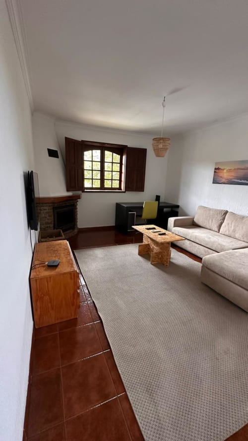 Sala de estar espaçosa da Quinta de Carvalhal em Guimarães com sofá bege, lareira e vista para o jardim através