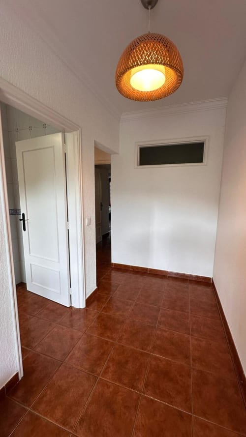 Corredor moderno na Quinta de Carvalhal, Guimarães, com piso em azulejos de barro, paredes brancas e luminária suspensa de madeira,