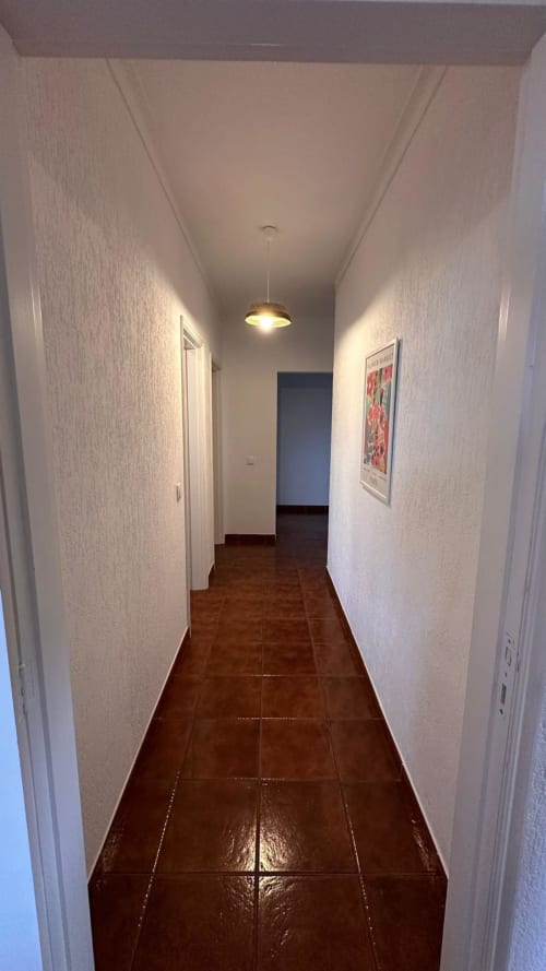 Corredor luminoso na Quinta de Carvalhal em Guimarães com paredes brancas, piso de azulejos marrom e pendente