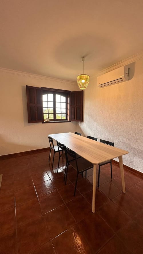Sala de jantar luminosa na casa de campo Quinta de Carvalhal em Guimarães com mesa de madeira, cadeiras pretas, luminária pendente e jardim