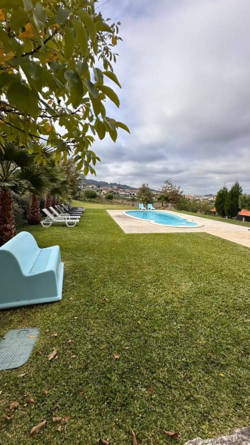 Jardim da Quinta de Carvalhal com piscina aquecida, espreguiçadeiras e vista para a serra de Guimarães sob céu nublado