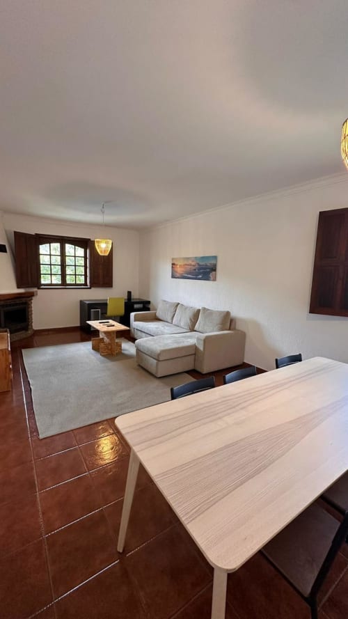 Ampla sala de estar e jantar da casa de hóspedes Quinta de Carvalhal, Guimarães, com sofá bege, mesa de madeira e vistas para o jardim