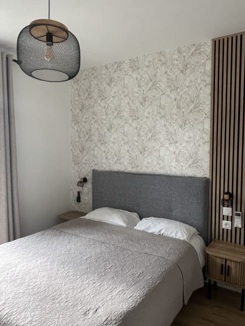 Chambre moderne à l'Hôtel Les Paquebots à Port-Vendres avec lit capitonné gris, papier peint botanique et luminaires suspendus.
