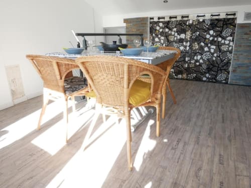Salle à manger lumineuse dans un appartement avignonnais avec chaises en rotin, table et vue sur la cuisine aux accents bleus.