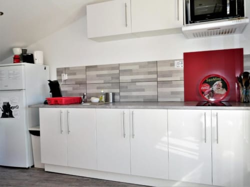 Cuisine moderne blanche avec crédence en carrelage gris, mur d'accent rouge et enseigne Coca-Cola à l'appartement Sweet Cotton Duplex, Avignon
