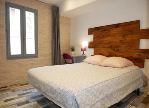 Chambre moderne avec tête de lit en bois, literie crème, murs en brique et vue sur la ville à Oriflamme & Travertin à Avignon