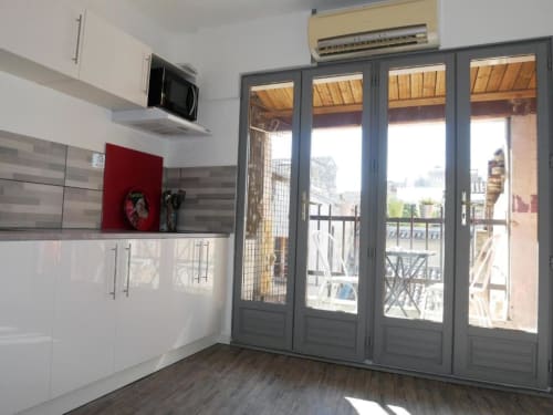 Cuisine moderne avec armoires blanches, crédence grise et grandes portes vitrées ouvrant sur un balcon avec vue sur la ville à Avignon