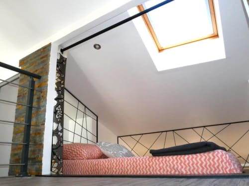 Chambre moderne dans un duplex avignonnais avec literie chevron rouge, puits de lumière, lit en métal noir et mur de briques apparentes