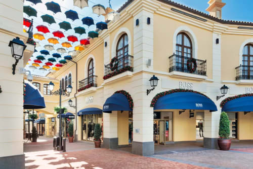 Colorful umbrellas above upscale shopping street in Málaga with cream buildings and blue awnings