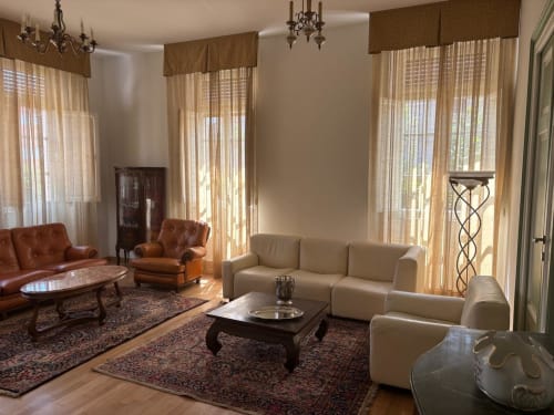 Elegante soggiorno dell'Il 900 B&B ad Avezzano con divano color crema, poltrone in pelle e arredi raffinati vicino alle finestre con tende trasparenti