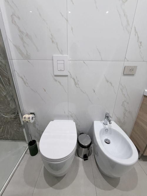 Bagno moderno a Sabò Bologna con rivestimento in marmo bianco, toilette, bidet e accessori
