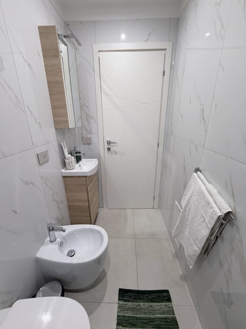 Bagno moderno a Sabò Bologna con pareti in marmo, lavabo bianco, bidet, portasciugamani e porta bianca