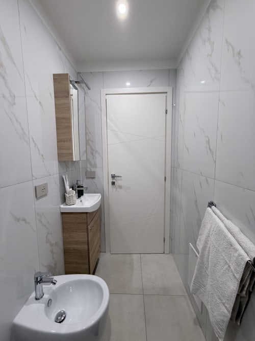 Bagno moderno in marmo a Sabò Bologna con lavabo bianco, mobile in legno, porta bianca e porta d'ingresso a Bologna
