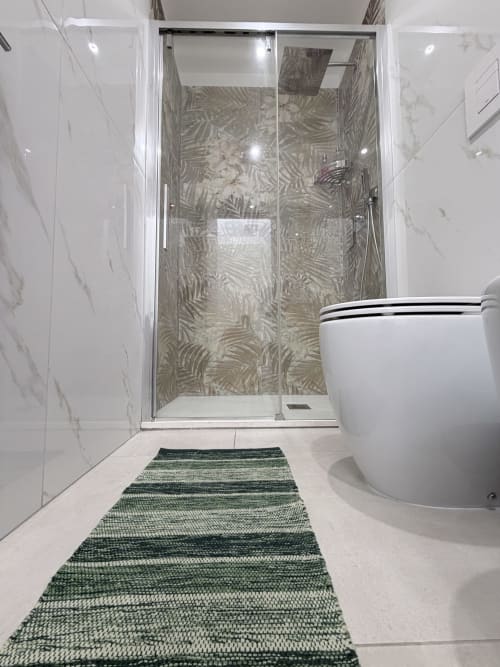 Bagno moderno a Sabò Bologna con doccia in vetro, piastrelle in marmo, wc bianco e tappetino da bagno a righe verdi