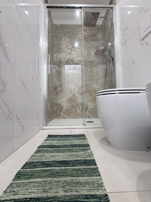 Bagno moderno a Sabò Bologna con pareti in marmo, box doccia in vetro con piastrelle decorate, wc e tappeto da bagno a righe verdi