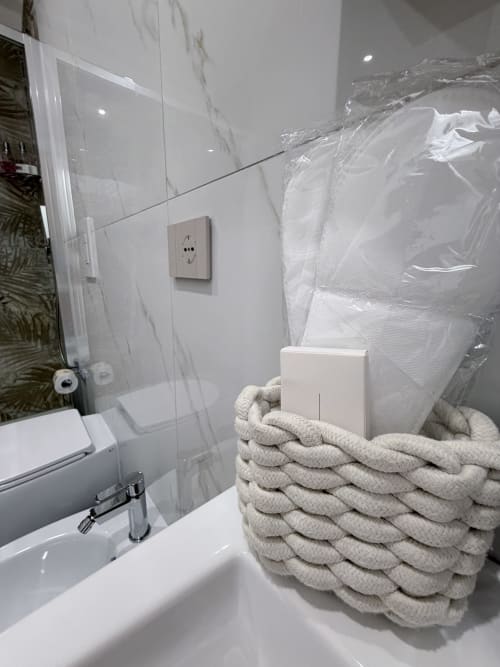 Bagno moderno a Sabò Bologna con pareti in marmo, lavabo bianco e cesto intrecciato con articoli da bagno e asciugamani