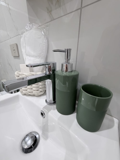 Lavabo moderno con dispenser di sapone verde e bicchiere presso l'hotel Sabò Bologna a Bologna, Italia