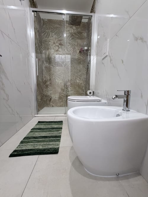 Moderno bagno di Sabò Bologna con lavandino rotondo bianco, cabina doccia in vetro, pareti in marmo, tappeto da bagno verde e piastrellato