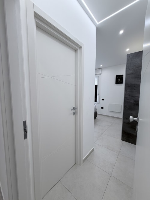 Corridoio moderno a Sabò Bologna con porte bianche, pannello scuro in accento e luci LED a soffitto nella camera Lame