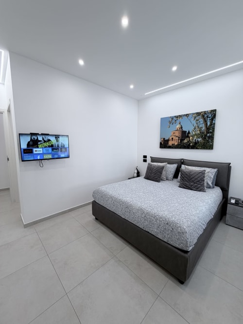Camera moderna a Sabò Bologna con letto nero, biancheria grigia, TV a parete e arte religiosa a Bologna, Italia