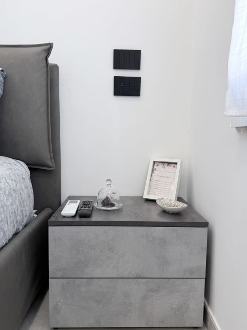 Elegante comodino grigio moderno con telecomando e oggetti decorativi accanto al letto imbottito scuro nella boutique hotel Sabò Bologna