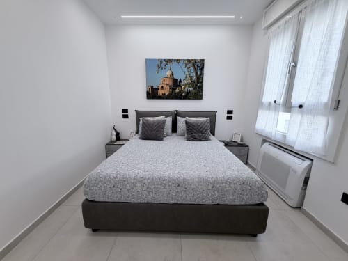 Camera moderna a Sabò Bologna con letto matrimoniale, biancheria grigia, comodini scuri e stampa architettonica sopra la testata