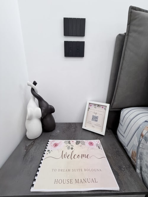 Cartello di benvenuto e manuale della casa per la guest house Dream Suite Bologna, con piccole statuette decorative in bianco e nero sul comodino
