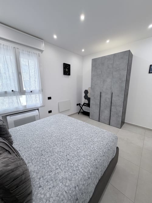 Camera moderna a Sabò Bologna con letto queen size, guardaroba grigio, finestra con vista cortile e arredi contemporanei