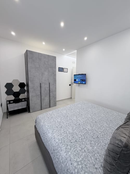 Camera moderna a Sabò Bologna con letto matrimoniale, guardaroba grigio, TV a parete e arredamento minimalista