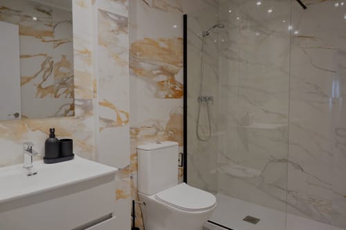 Baño moderno en Palacio Mambrilla con paredes de mármol, ducha a ras de suelo, lavabo blanco e inodoro en apartamento de Valladolid