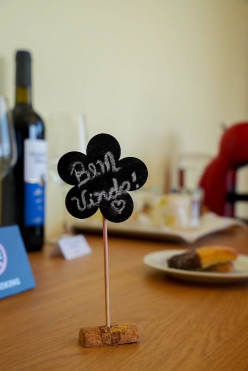 Placa em lousa formato flor preta com a inscrição "Bom Vindo" sobre mesa de vinho na Tranca da Barriga Casa do Vinho