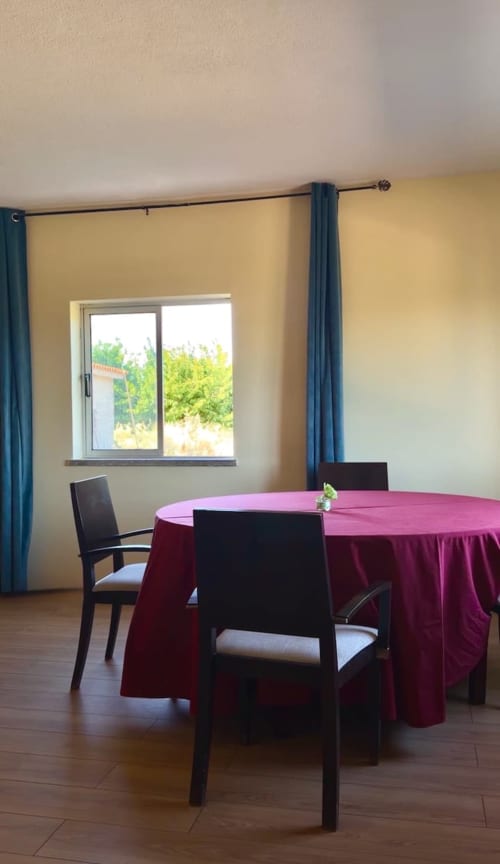 Sala de jantar em Tranca da Barriga com mesa redonda, toalha de mesa bordô, cadeiras pretas e vista para as montanhas pelos painéis deslizantes