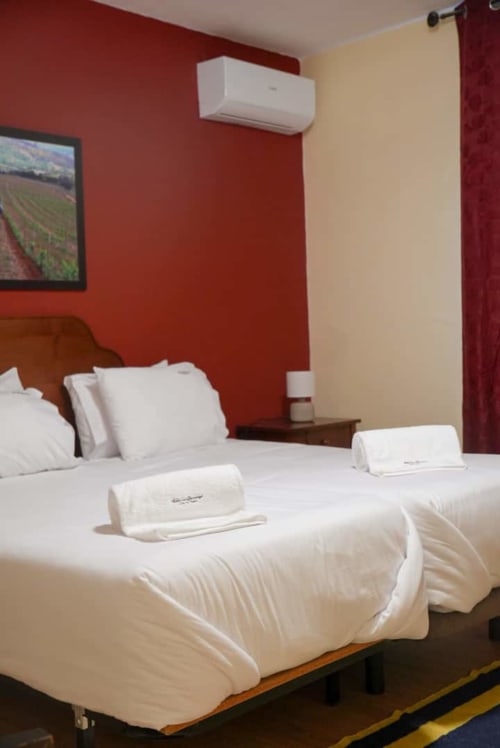 Quarto limpo da casa de hóspedes Tranca da Barriga Casa do Vinho com camas de solteiro, parede vermelha e ar-condicionado