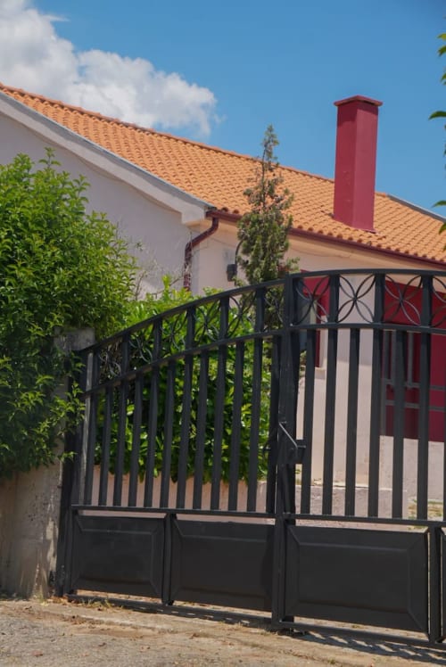 Portão de ferro preto da entrada de Tranca da Barriga Casa do Vinho em Dominguiso, Portugal, com telhado de terracota