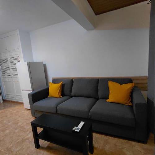 Sala de estar moderna con sofá gris, almohadas amarillas, mesa de centro negra y viga de madera en la cabaña El Palm-Mar.