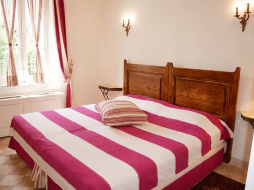 Chambre double lumineuse à l'Auberge du Parc avec lit aux rayures rose et blanc, tête de lit en bois et vue sur le jardin