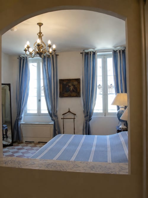 Élégante chambre double à l'Auberge du Parc avec literie rayée bleue, portail voûté, lustre en laiton et vue sur le jardin