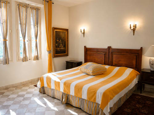 Chambre lumineuse à l'Auberge du Parc à Correns avec literie jaune rayée, tête de lit en bois et vue sur le jardin