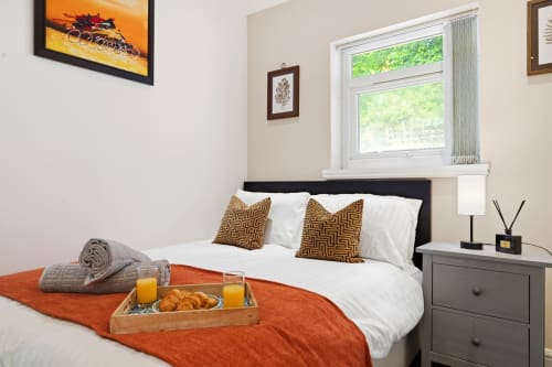 Modern bedroom at 11.11 Property Estates Birmingham with bed, breakfast tray, orange throw, and city view window